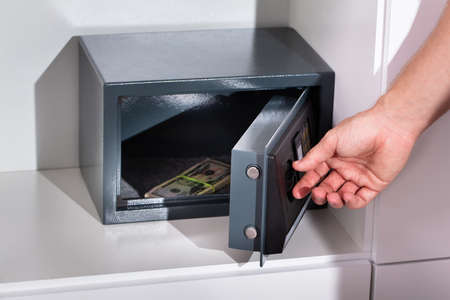 A Man's Hand Putting Bundle Of Banknote In A Safe Deposit Box