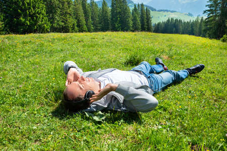 Man Relaxing Lying In Field Of Grass Listening Music In Mountainsの写真素材