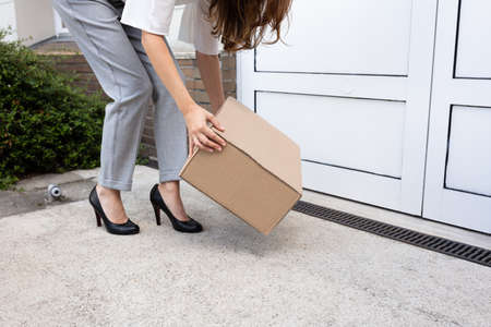 Smiling Young Woman Peeking Up The Delivered Parcel At The Door Entranceの写真素材