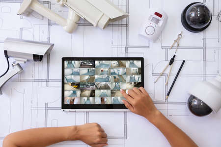 Close-up Of A Person Watching Footage On Laptop  With Security Equipment On Blueprint
