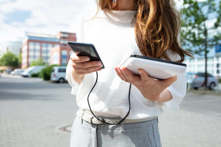 Closeup Of Woman Holding Mobile Phone And External Batteryの写真素材