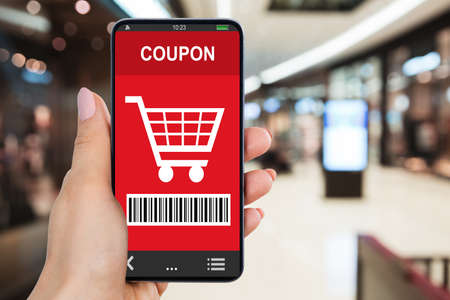 Close-up Of Woman's Hand Holding Smartphone With Shopping Coupon In Mall