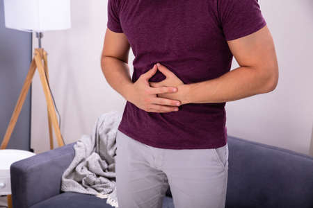 Midsection Of Man Suffering From Stomach Ache Standing Near Sofaの写真素材