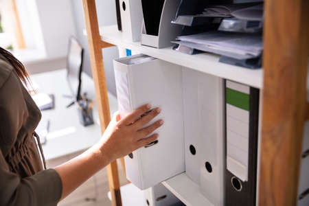Businessperson's Hand Taking Folder From Wooden Shelf In Officeの写真素材