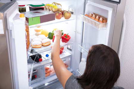 Rear View Of A Young Woman Taking Food From Refrigeratorの写真素材