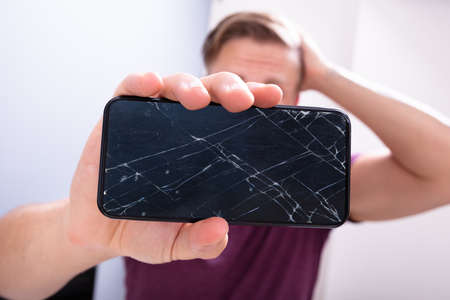 Worried Man Holding Broken Smartphone At Home