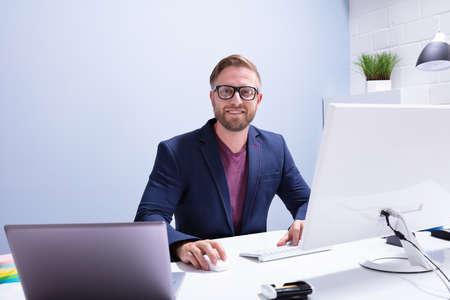 Portrait Of A Young Businessman Sitting In Front Of Computer At Workplaceの写真素材