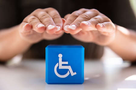 Close-up Of A Person's Hand Protecting Blue Cubic Block With Disabled Icon
