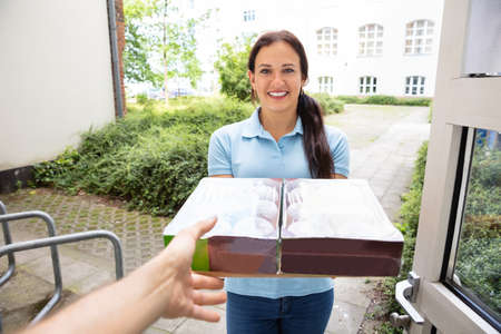 Man Receiving Donuts From Delivery Woman At Homeの写真素材