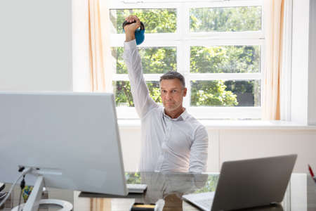 Businessman Exercising With Kettlebell In Office During Break