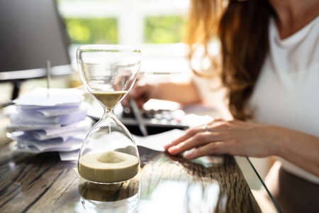 Close-up Of A Hourglass In Front Of Businesswoman Working In Officeの写真素材