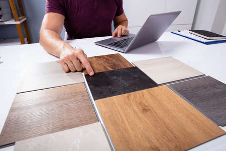 Male Interior Designer Choosing Color Of Tiles With Laptop Working At Workplace