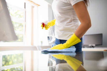 Side View Of Female Janitor Cleaning Desk With Blue Napkin In Officeの写真素材