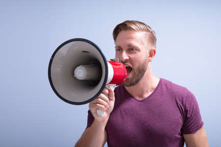 Close-up Of A Beard Man Shouting Through A Megaphone Against Gray Backgroundの写真素材