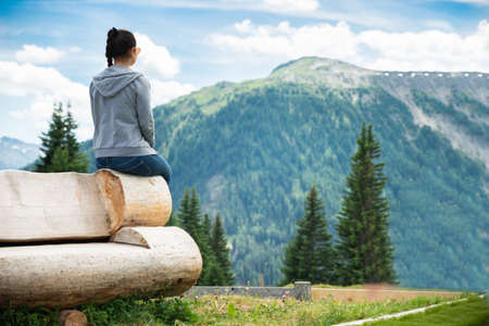 Woman Sitting On Bench Enjoying Panoramic Mountain Viewの写真素材
