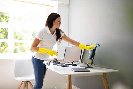 Young Woman Cleaning Computer With Blue Napkin In Officeの写真素材