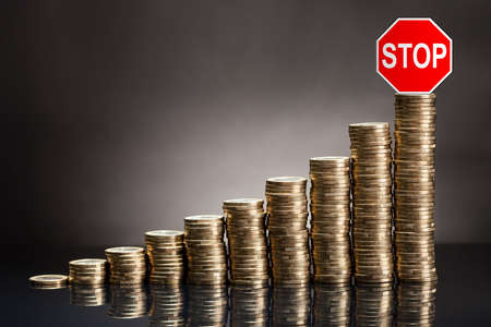 Rising Stack Of Coins With Red Stop Caution Against Checkered Background