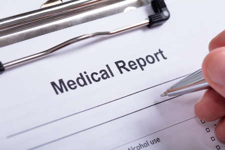 Overhead View Of Human Hand Holding Pen With Medical Report On Clipboard Over White Backgroundの写真素材
