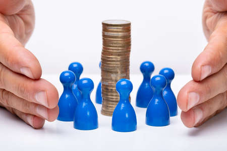 Businessperson Protecting Stacked Coins And Human Figures