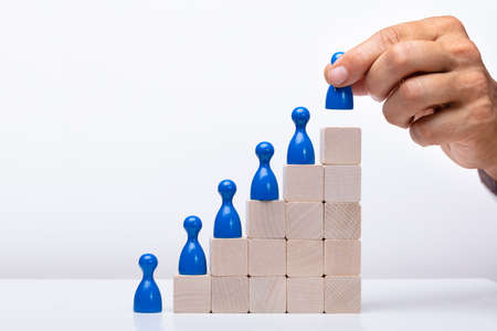 Businessperson Placing Blue Human Figure On Top Of Wooden Block