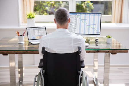 Handicapped Businessman Sitting On Wheelchair And Using Computer In Office