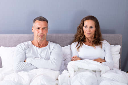 Portrait Of Sad Couple Sitting On Bed With White Blanketの写真素材