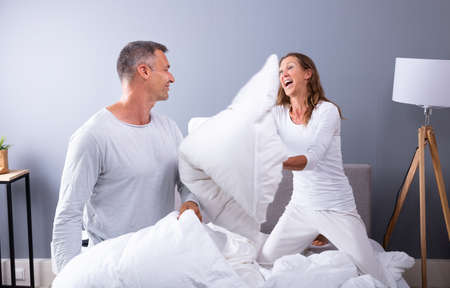 Happy Couple Fighting Together With White Pillows On Bedの写真素材