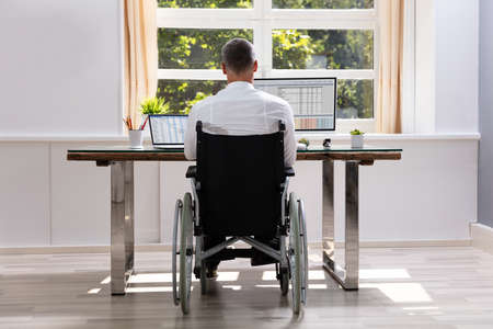 Handicapped Businessman Sitting On Wheelchair And Using Computer In Officeの写真素材