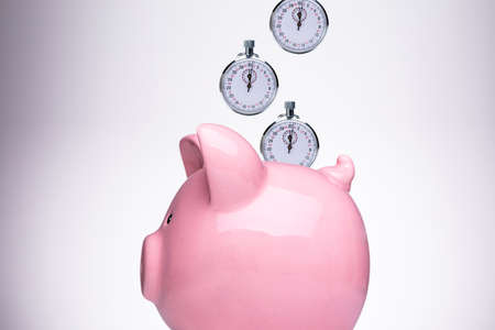Close-up Of Pink Piggy Bank With Stopwatch Against White Backgroundの写真素材
