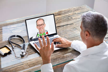 Close-up Of Doctor Having Video Conference On Laptop At Wooden Deskの写真素材