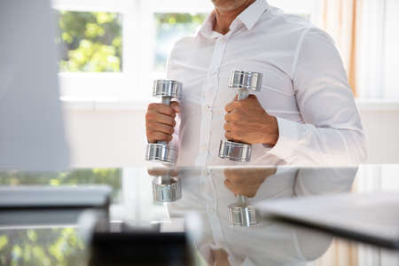 Businessman Exercising With Dumbbells In Office During Break
