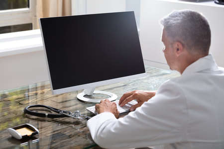 Confident Male Doctor Working On Computer At Deskの写真素材