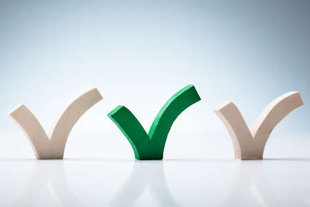 Green Check Mark In Between Wooden Check Marks Over White Desk Against Wallの写真素材