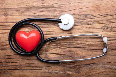 Close-up Of A Red Heart With Stethoscope On Wooden Deskの写真素材