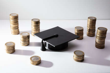 Black Graduation Hat With Golden Stacked Of Coins On White Backgroundの写真素材