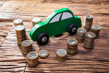 Green Wooden Car Near The Stack Of Coins On Wooden Deskの写真素材