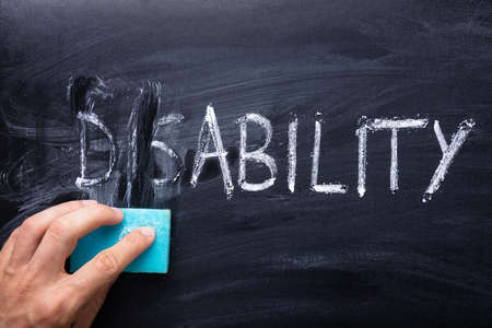 Man's Hand Erasing Dis Text From Disability Word With Sponge Over Blackboard