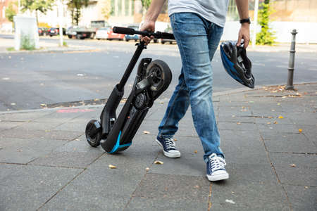 Man Carrying E-Scooter Walking On Street To Work