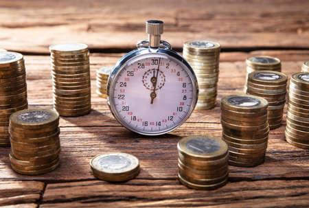 Stacking Golden Coins On Desk Near Stopwatch Over Wooden Deskの写真素材