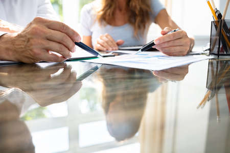 Mid- Section Of Two Businesspeople Analyzing Graph Over Office Deskの写真素材