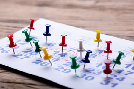 Calendar With Circular Mark Around 14 Number And Colorful Push Pins Over Wooden Deskの写真素材