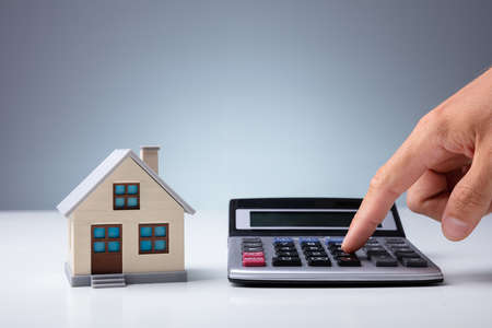 Person's Hand Calculating With Calculator Near House Model On Deskの写真素材