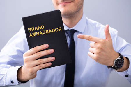 Man Holding Book With Brand Ambassador Text And Pointingの写真素材
