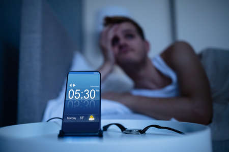 Man Waking Up With Alarm On Mobile Phone At Homeの写真素材