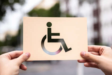 Hands Holding Paper With Cutout Disabled Sign Outdoorsの写真素材