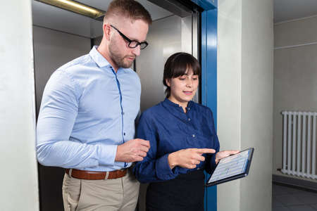 Portrait Of A Businessman And Businesswoman Standing In Elevator Discussing The Project On Digital...