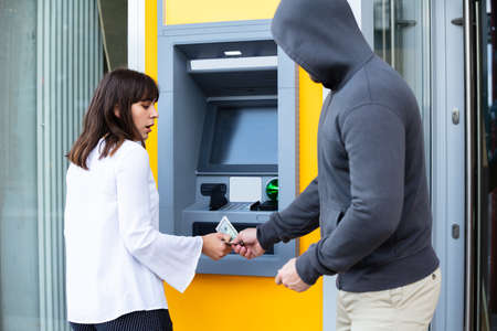 Shocked Young Woman Looking At Thief Stealing Her Money Standing Near The ATM Machineの写真素材