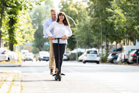 Portrait Of Happy Couple Riding On Electric Scooter Over The Street In The Cityの写真素材