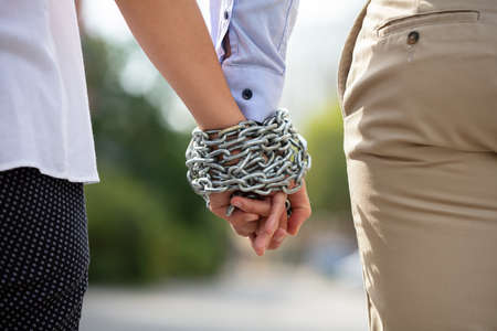 Rear View Of Couple's Hand Tied With Metal Chain At Outdoors