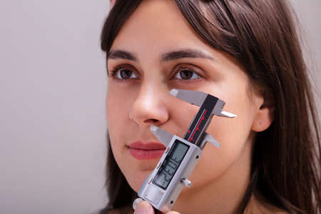 Doctor Measuring Proportions Of Female Nose While Using Calipers In Clinic